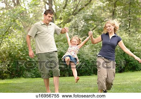 Stock Photography - Young couple swinging child while walking, Regina, Saskatchewan. Fotosearch
