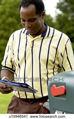 Stock Image - African American man getting mail from mailbox. Fotosearch