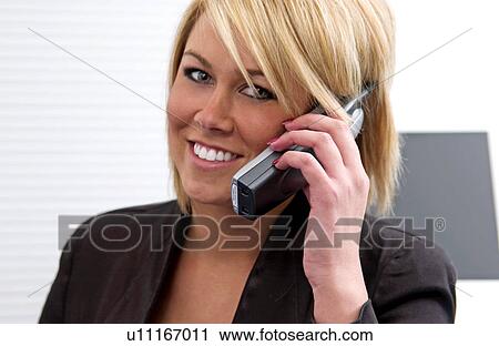 Stock Image - Businesswoman at desk talking on cordless phone. Fotosearch