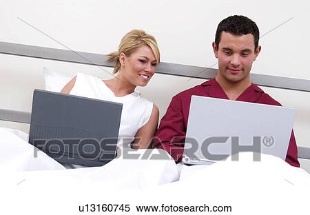 Stock Photography - Couple in bed working on laptop computers. Fotosearch