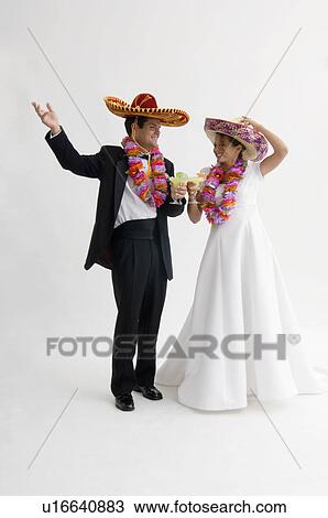 Stock Image - Bride and groom wearing sombreros and leis and holding margarita. Fotosearch