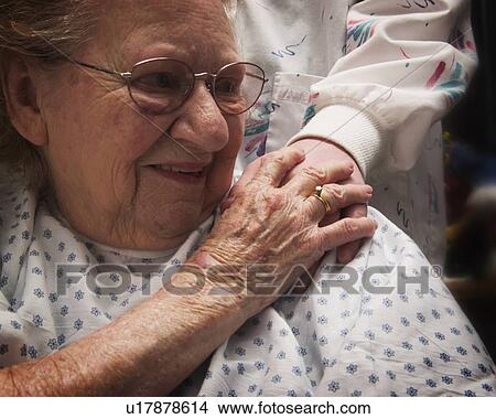 Picture - Senior woman in wheelchair holding hands with nurse. Fotosearch