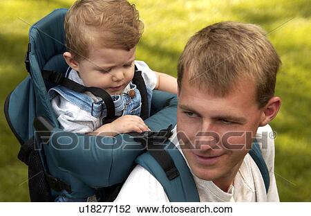 Stock Image - Father carrying son in backpack hiking on walk. Fotosearch