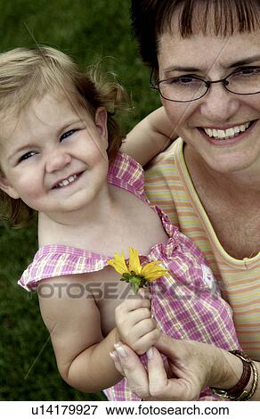 Stock Photo - Grandmother holding a toddler with a flower in her hand. Fotosearch