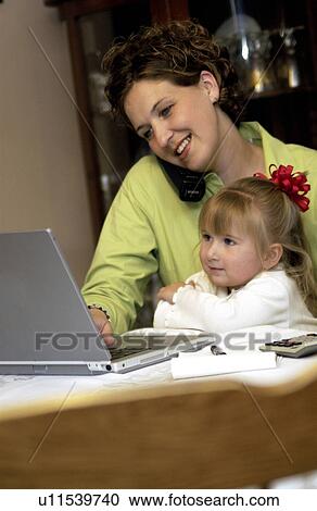 Mom working at home while holding daughter View Large Photo Image Stock Image - Mom working at home while holding daughter. Fotosearch