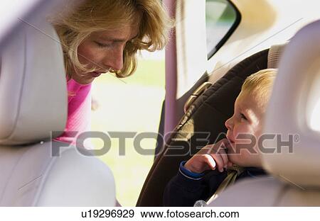 Stock Photo - Mother putting child in car seat. Fotosearch