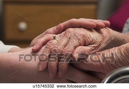 Stock Image - Senior woman in wheelchair holding hands with woman. Fotosearch
