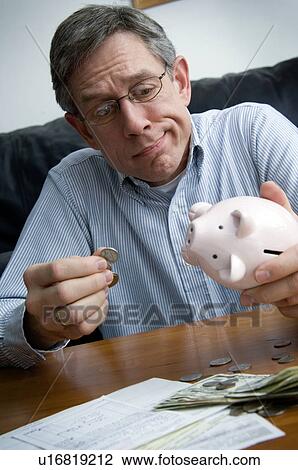 Stock Image - Man raiding piggy bank. Fotosearch
