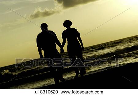 Stock Image - Couple holding hands and walking on beach. Fotosearch