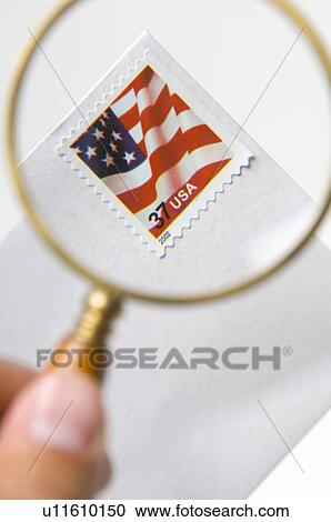 Stock Image - Man holding magnifying glass over US stamp. Fotosearch