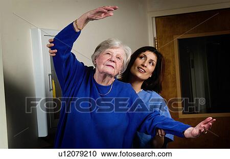 Stock Image - Nurse helping senior woman with exercising. Fotosearch
