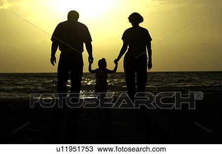 Stock Image - Couple walking with child on beach. Fotosearch