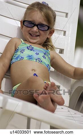 Stock Image - Little girl sitting in a chair by a pool. Fotosearch