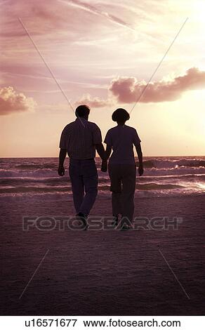 Couple holding hands and walking on beach View Large Photo Image Stock Photo - Couple holding hands and walking on beach. Fotosearch