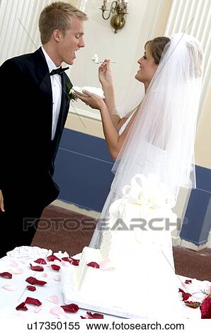 Stock Photography - Bride and groom at reception feeding each other wedding cake. Fotosearch