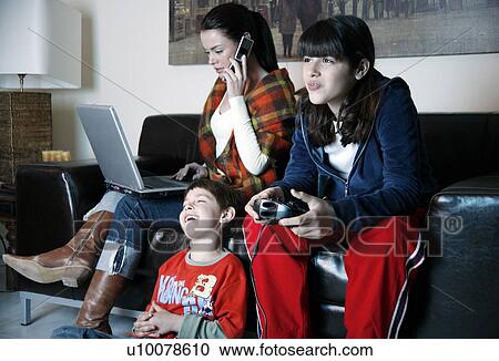 Stock Image - Mother works on laptop while children play video game. Fotosearch
