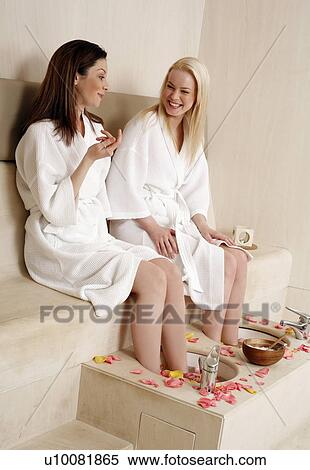 Stock Photography - Two young women enjoying a foot bath with rose petals. Fotosearch
