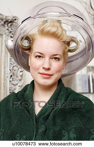 Stock Image - Young woman sitting under hairdryer. Fotosearch