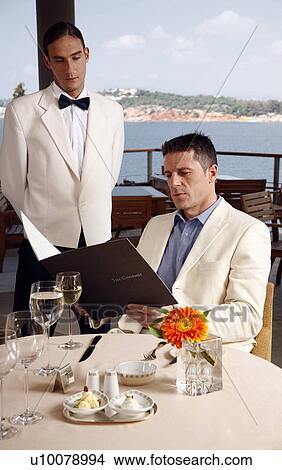 Picture - Man reading menu in restaurant, waiter waiting.. Fotosearch