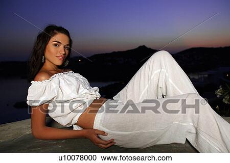 Stock Image - Woman in white outfit on terrace with a view. Fotosearch