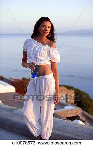 Stock Image - Woman in white outfit on terrace with a view. Fotosearch