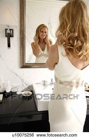 Stock Photograph - Woman looking at herself in the bathroom mirror. Fotosearch
