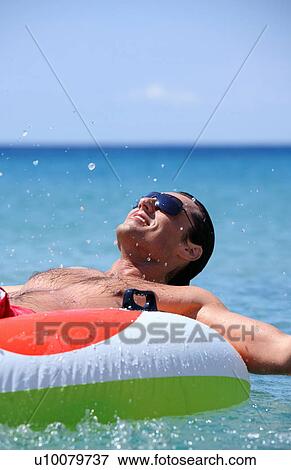 Stock Photo - Young man in water on inflatable life ring. Fotosearch