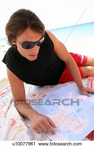Stock Image - Young man on beach reading map. Fotosearch