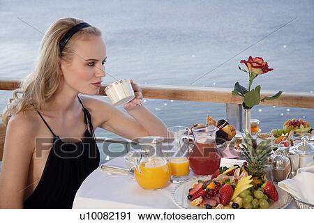Stock Image - Young woman having breakfast on hotel terrace. Fotosearch