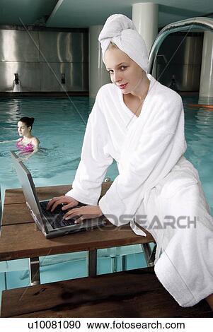 Stock Image - Woman on computer next to a swimming pool. Fotosearch