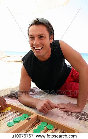 Stock Photo - Young man on beach playing backgammon. Fotosearch