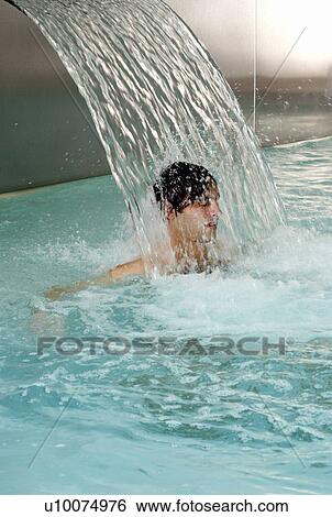 Young man standing under water spray in spa pool View Large Photo Image Stock Photograph - Young man standing under water spray in spa pool. Fotosearch