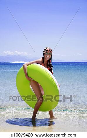 Stock Image - Young woman on beach with inflatable life ring. Fotosearch