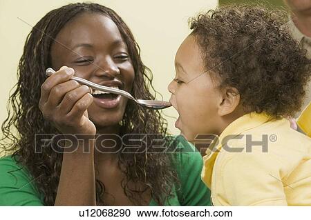 Stock Image - AA feeding, giving medicine to her Mulatto boy 1. 5 years old.. Fotosearch