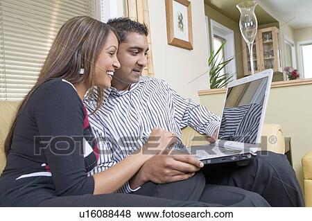 Stock Photo - Couple on sofa with laptop, Winnipeg, Canada. Couple appear to be of Indian ethnicity.. Fotosearch