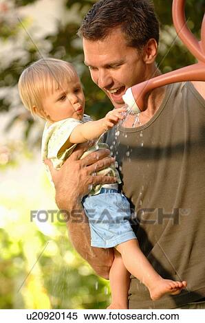 Stock Photography - Dad & baby playing with watering can, Regina, Saskatchewan. Fotosearch