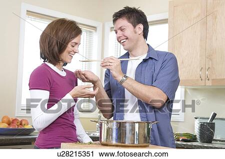 Stock Image - Man offers spoon for woman to taste, Winnipeg, Canada. Fotosearch