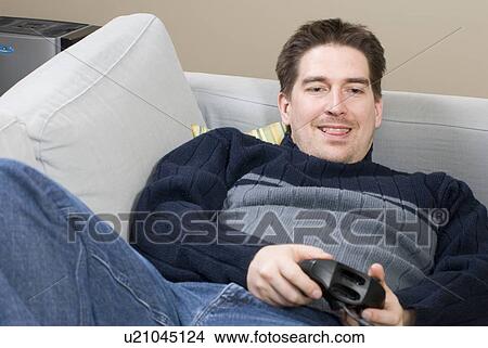 Picture - Man reclines on sofa with game console. Fotosearch