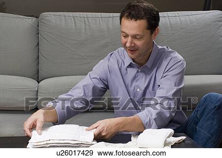 Stock Photo - Man seated on floor by sofa folding cloth diapers, Winnipeg, Canada. Fotosearch