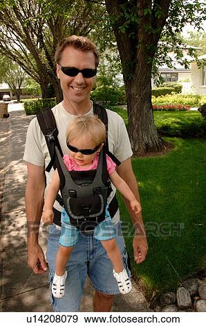 Stock Photo - Man walking down street carrying baby in snuggly, Regina, Saskatchewan. Fotosearch