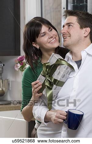Stock Photo - Woman giving man gift, wrapped in newsprint with reusable fabric ribbon. Wrapping gifts in comics, newsprint, or old maps eliminates the waste of wrapping paper, Winnipeg, Canada. Fotosearch