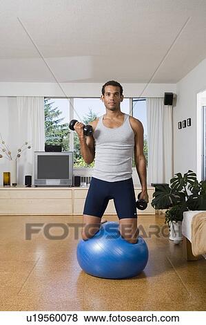 Young Man at home kneels on exercise ball while lifting weights, Vancouver, British Columbia View Large Photo Image Stock Photo - Young Man at home kneels on exercise ball while lifting weights, Vancouver, British Columbia. Fotosearch