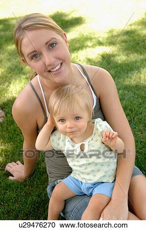 Stock Image - Young woman w/baby in grass, Regina, Saskatchewan. Fotosearch