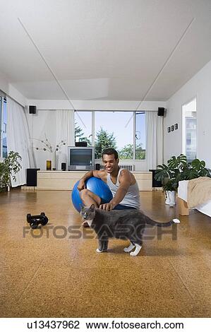 Stock Image - Young Man at home pets cat before exercising, Vancouver, British Columbia. Fotosearch