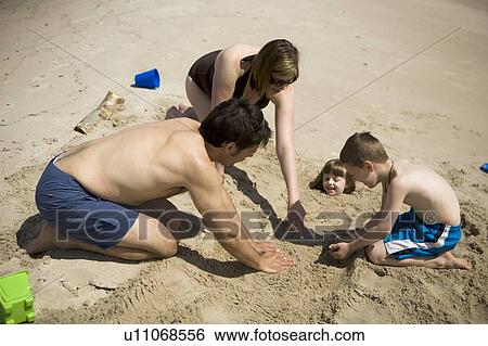 Stock Photograph - Family buried girl (4) in the sand, Grand Beach Provincial Park, Manitoba, Canada. Fotosearch