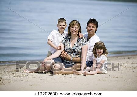 Stock Image - Family of four seated at shore, Grand Beach Provincial Park, Manitoba, Canada. Fotosearch