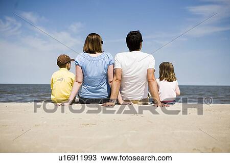 Stock Image - Family of four seated on beach with backs to camera, Grand Beach Provincial Park, Manitoba, Canada. Fotosearch