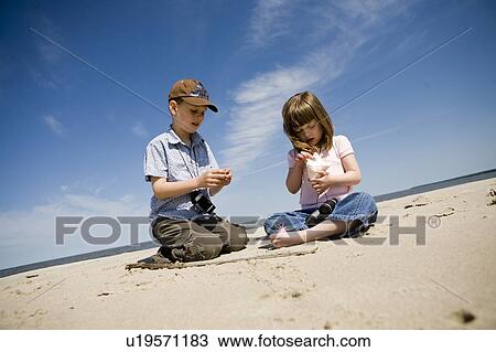 Stock Image - Four year old girl and seven year old boy look at shells, Grand Beach Provincial Park, Manitoba, Canada. Fotosearch