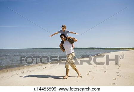 Stock Photo - Man carries boy (7) on his shoulders as boy holds arms out, Grand Beach Provincial Park, Manitoba, Canada. Fotosearch