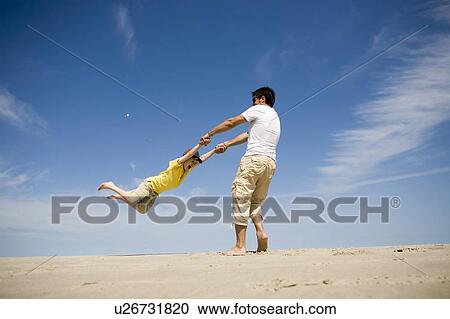 Stock Image - Man swings boy (7) in circle, Grand Beach Provincial Park, Manitoba, Canada. Fotosearch